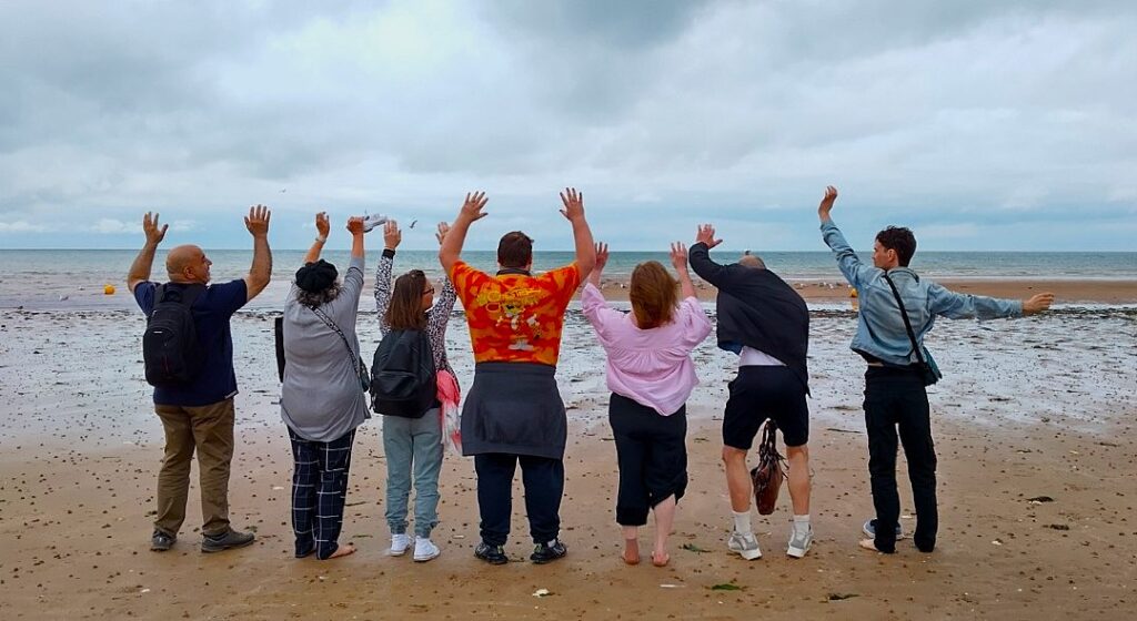 Seven people facing the sea with backs towards the camera and arms up.