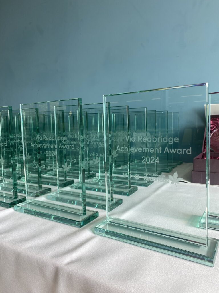 Glass awards presented on a table, etched with the words 'Via Redbridge Achievement Award 2024'