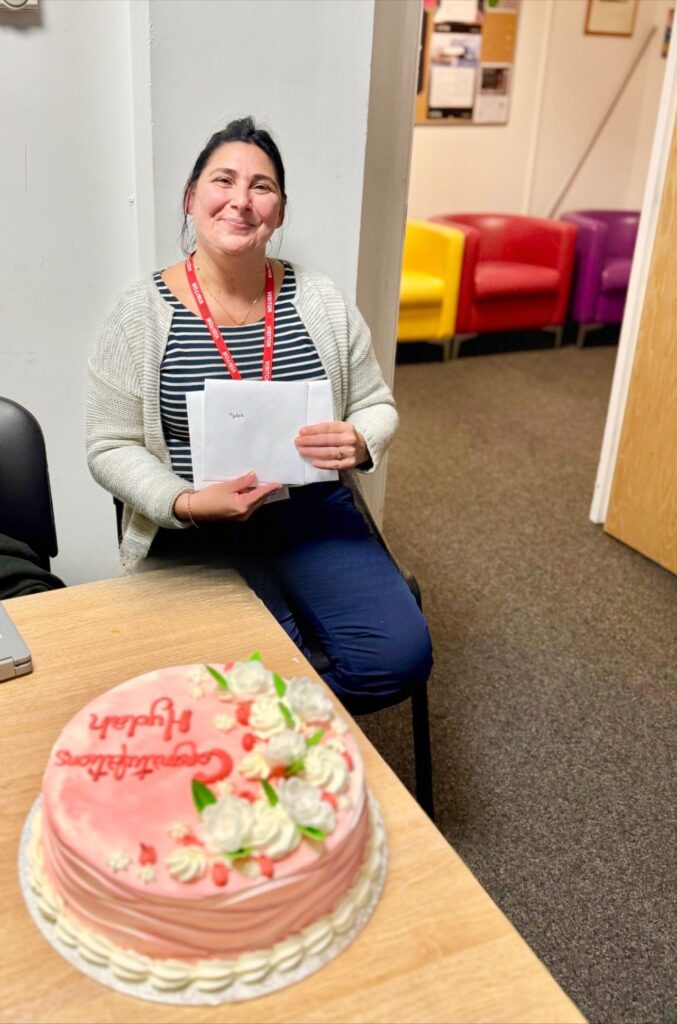 person smiling and sat down holding envelopes with a pink cake in front